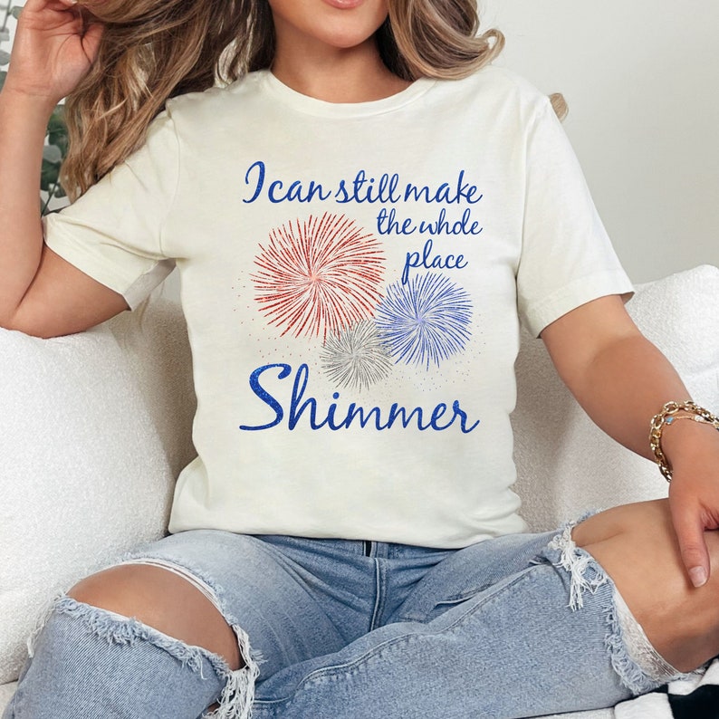 May include: A white t-shirt with a red, white, and blue firework graphic and the text "I can still make the whole place shimmer".