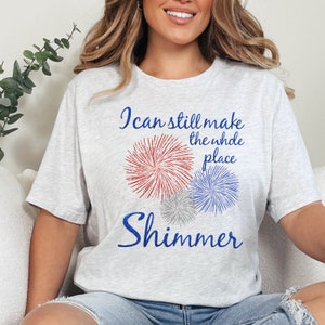 May include: A gray t-shirt with a blue and red firework graphic and the text "I can still make the whole place shimmer".