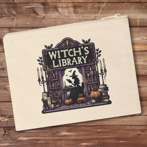 May include: A beige canvas zippered pouch featuring a colourful illustration of a witch's library. The illustration depicts a witch reading a book in a library with shelves full of books, candles, and pumpkins. The text "Witch's Library" is displayed on a sign above the library.