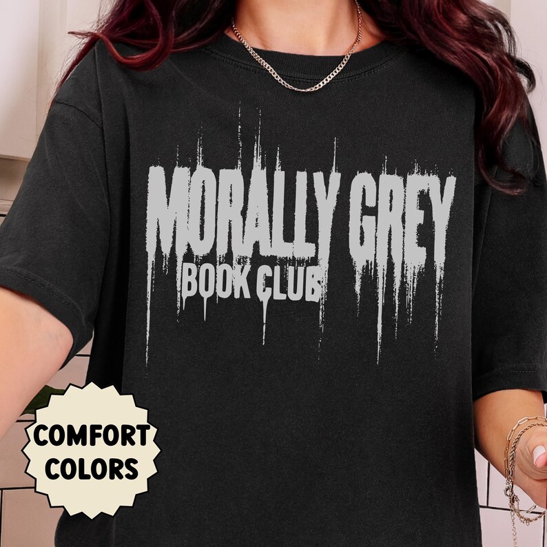 May include: Black t-shirt with the text "MORALLY GREY BOOK CLUB" in distressed white lettering. The shirt also has a "COMFORT COLORS" tag. The shirt is a dark color and appears to be made of a soft material.