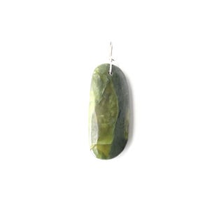 May include: A green and gray jade pendant with a silver-colored hook. The polished stone has a smooth, oblong shape with variations in color and texture. The pendant is displayed against a white background.