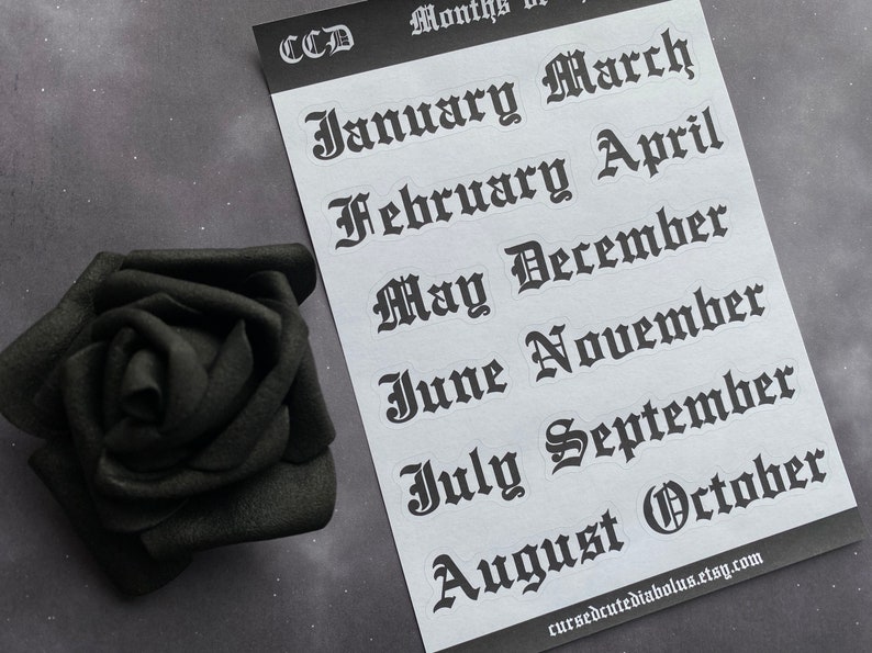 May include: A sheet of white paper with black gothic font stickers of the months of the year. The stickers are arranged in two rows. The text on the stickers reads: January, March, February, April, May, December, June, November, July, September, August, October. The text at the bottom of the sheet reads: cursedcutediabolus.etsy.com