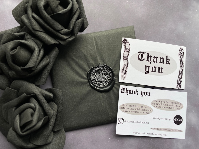 May include: A thank you card with a black and white snake design. The card has the text "Thank you" in a gothic font. The card also includes the text "Don't forget to tag me in pictures on social media and leave a review on Etsy!" and "Thank you for supporting my small business! It really means the world to me!"  The card also includes the text "Spooky blessings, CCD" and the website address "www.cursedcutediabolus.etsy.com".