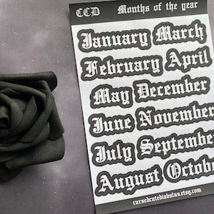May include: A sheet of white stickers with the months of the year written in a gothic font. The stickers are black and white and have a slightly distressed look. The text on the stickers reads: "January, March, February, April, May, December, June, November, July, September, August, October".