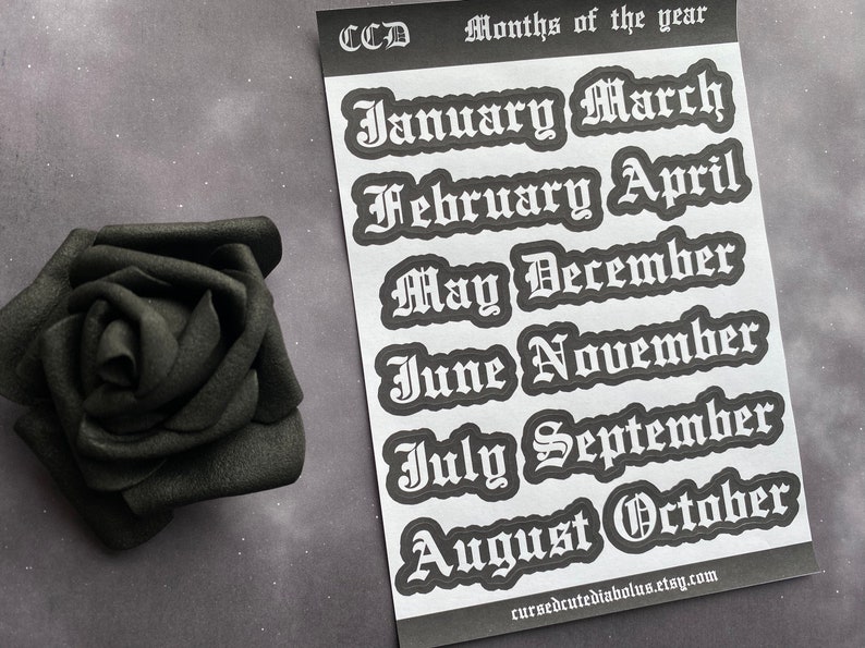 May include: A sheet of white stickers with the months of the year written in a gothic font. The stickers are black and white and have a slightly distressed look. The text on the stickers reads: "January, March, February, April, May, December, June, November, July, September, August, October".