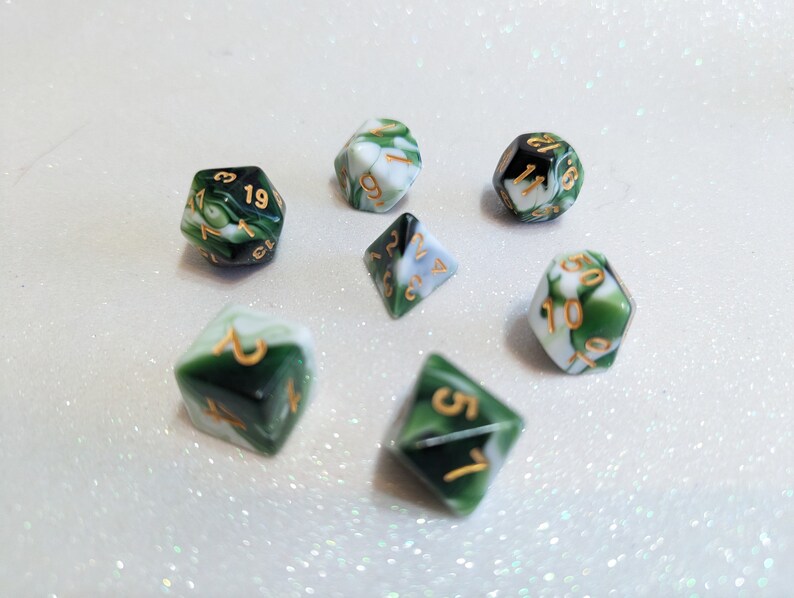 May include: Set of seven green and white dice with gold numbers. The dice are made of a marbled plastic material.