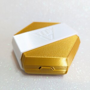 May include: A gold hexagonal box with a white lid. The lid has a geometric design and the box has a textured surface.