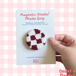 May include: A circular magnetic phone grip featuring a textured white and maroon checkered pattern. The product is mounted on a white display card with the text Magnetic Kindle/Phone Grip, MagSafe Compatible, and oodlesanddoodlesgb.etsy.com.