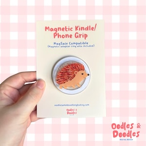 May include: A phone grip with a cartoon hedgehog design. The grip is MagSafe compatible and includes a magnetic adapter ring. The card also features the text "Magnetic Kindle/Phone Grip" and the shop's name.