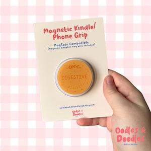 May include: A magnetic phone grip with a "Digestive Biscuit" design. The round grip is orange with the word "DIGESTIVE" and "BISCUIT" printed on it. The grip is on a cream-colored card with text that reads "Magnetic Kindle/ Phone Grip".