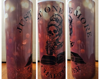 May include: A white tumbler with a red and brown background featuring a skull with a bun drinking from a cup. The text "Just One More Chapter" is printed on the tumbler.