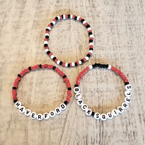 Set of 3 Haverford beaded bracelets. The first is red and white color blocked with Black Squirrels lettering. The second is red with black accents with Haverford lettering. The third is red, black and white beads