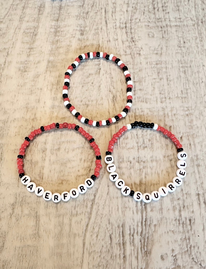 Set of 3 Haverford beaded bracelets. The first is red and white color blocked with Black Squirrels lettering. The second is red with black accents with Haverford lettering. The third is red, black and white beads