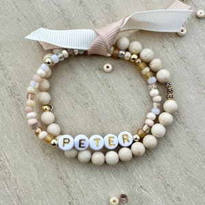May include: A white beaded bracelet with gold accents and the name "PETER" spelled out in white beads with gold lettering.