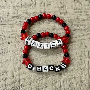 May include: Two red and black beaded bracelets with white letter beads spelling out the names "BAXTER" and "D-BACKS".