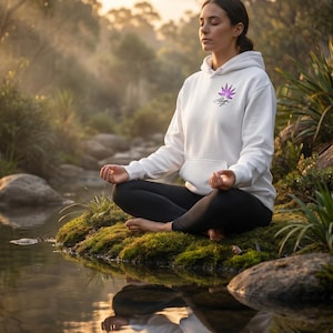 May include: A white hooded sweatshirt featuring a purple lotus flower graphic and the word Align printed on the chest. The garment has long sleeves, a front kangaroo pocket, and a drawstring hood, worn with black leggings while sitting in a pose.