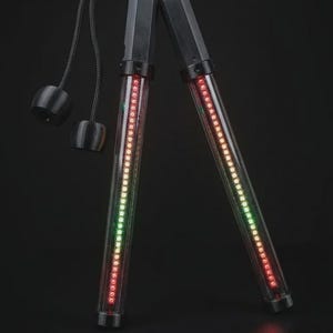 Peut inclure: Une paire de nunchakus composée de tubes cylindriques transparents contenant des rangées verticales de petites lumières LED multicolores rouges, orange et vertes. Les poignées sont noires, reliées par des cordons noirs avec deux poids noirs.