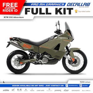 以下が含まれることがあります： 緑とオレンジのKTM 990アドベンチャーバイクに、地形図のデザインのデカールキットが貼られています。 デカールキットはオリーブグリーンで入手可能です。 画像には、「FREE CUSTOM RIDER ID」、「PRO MX GRAPHICS」、「DECALLAB since 2010」、「FULL KIT」、「Top-rated seller」、「KTM 990 Adventure」、「990」、「L」、「DESIGN AVAILABLE ON ANY BIKE - JUST CONTACT US!」、「decallaboratory」、「decallab」、「KIM」、「YAMAHA」、「can-am」、「Husqvarna」、「HUSABERG」、「GASGAS」、「BucciFoto」、「TOPO (olive)」のテキストが含まれています。