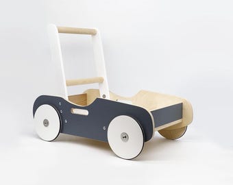 Op de afbeelding: Een witte en grijze houten loopwagen met een handvat en wielen. De loopwagen heeft een opbergvak aan de achterkant.