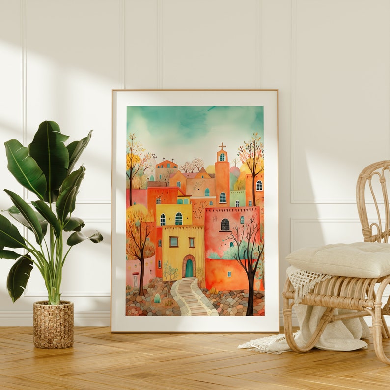 May include: A watercolor painting of a colorful village with a stone pathway leading up to a building with a cross on top. The buildings are painted in shades of orange, yellow, and red, with green accents. The painting is framed in a wooden frame.