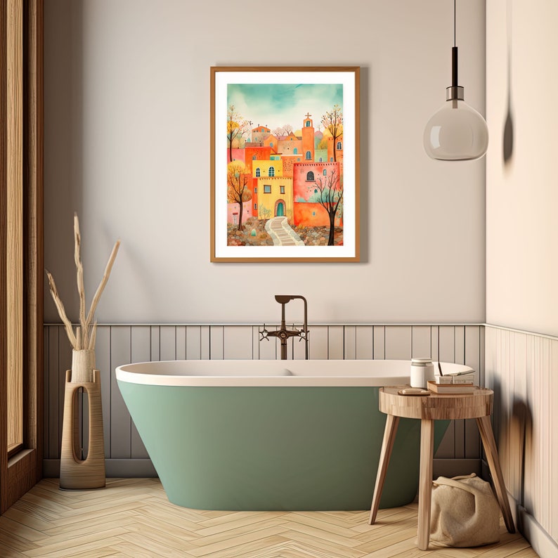 May include: A watercolor painting of a colorful village with a path leading to a building with a blue door. The painting is framed in a wooden frame and is hanging on a wall in a bathroom.
