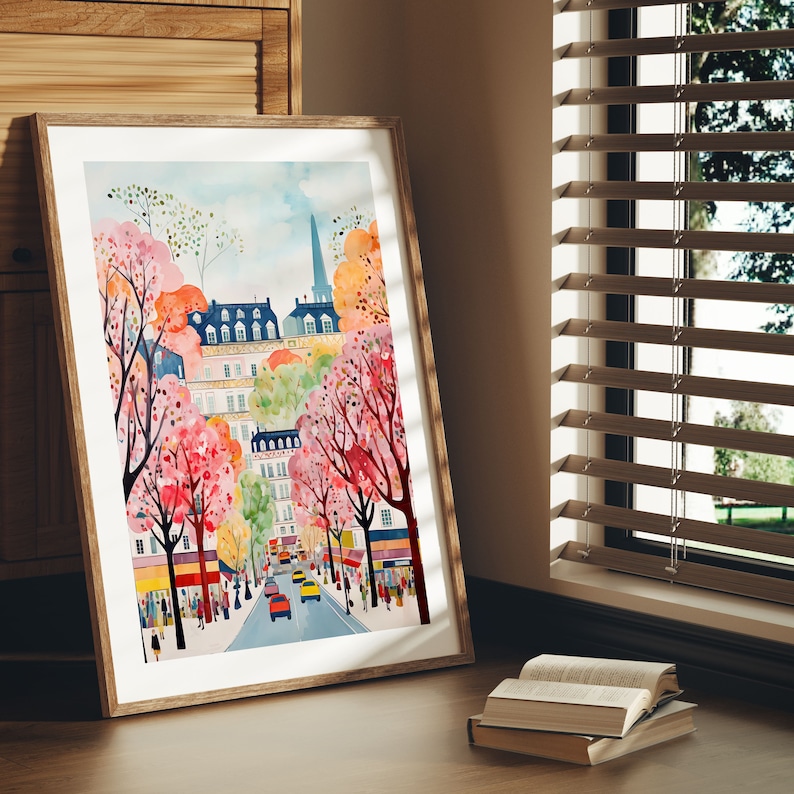 May include: A watercolor painting of a city street scene with buildings and trees. The trees have pink and purple flowers. There are cars driving down the street. The painting is framed in a light brown frame.
