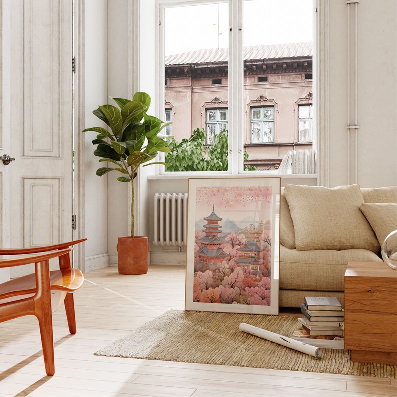May include: A framed print of a Japanese pagoda surrounded by cherry blossom trees. The print is hanging on a white wall in a living room with a beige couch, a wooden coffee table, and a potted plant.