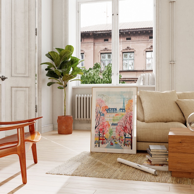 May include: A framed watercolor painting of a city street scene with pink and white flowering trees. The painting is in a gold frame and is hanging on a white wall.