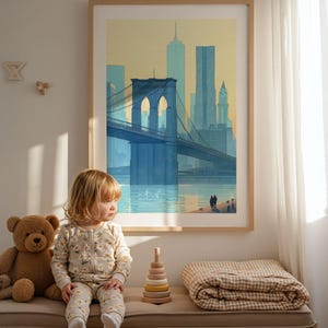 Puede incluir: Una impresi&oacute;n enmarcada del puente de Brooklyn en tonos azules y amarillos cuelga sobre un banco. Un ni&ntilde;o con un mono floral est&aacute; sentado en el banco junto a un oso de peluche, un juguete apilable de madera y una manta doblada.
