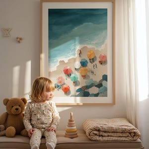 May include: A framed watercolor print depicts a beach scene with colorful umbrellas and people. A young child in a daisy-print onesie sits on a bench next to a teddy bear, a wooden stacking toy, and a folded blanket. The artwork is in a light wood frame.