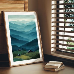 May include: A framed art print featuring a watercolor landscape of layered blue mountains. The artwork depicts rolling hills with small buildings in the foreground. The frame is made of light-colored wood, and the print is leaning against a wall near a window.