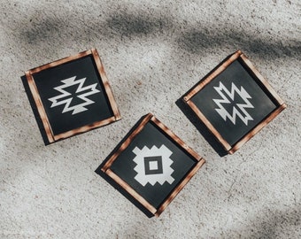 Może przedstawiać: Trzy drewniane podkładki pod kubki z czarnym tłem i białymi geometrycznymi wzorami. Podkładki są ułożone w kształt trójkąta na jasnoszarym tle.