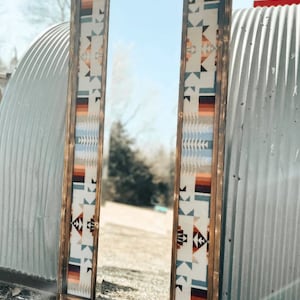 Puede incluir: Un espejo con marco de madera y un borde de tela con un patrón de estilo suroeste. El espejo está de pie frente a una pared de metal corrugado.