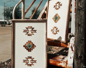 Puede incluir: Dos letreros de madera con fondo blanco y diseños geométricos marrones. Los diseños presentan acentos turquesa. Los letreros están apoyados en una barandilla de metal oxidado.