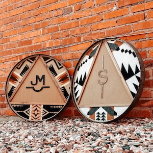 May include: Two round wooden signs with a geometric pattern in black, white, and brown. One sign has the letters "JM" in the center, and the other sign has a dollar sign in the center.