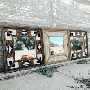 May include: Three wooden framed mirrors with geometric patterns in black, white, and brown. The mirrors are arranged in a row on a gray wooden wall.
