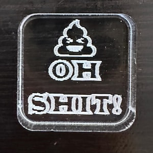 May include: A clear plastic badge with a white poop emoji and the text "OH SH*TS" in white.