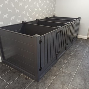 May include: A grey wooden pet crate with multiple compartments. The crate has a slatted design on the front and is hinged. The background features a dog-themed wallpaper.