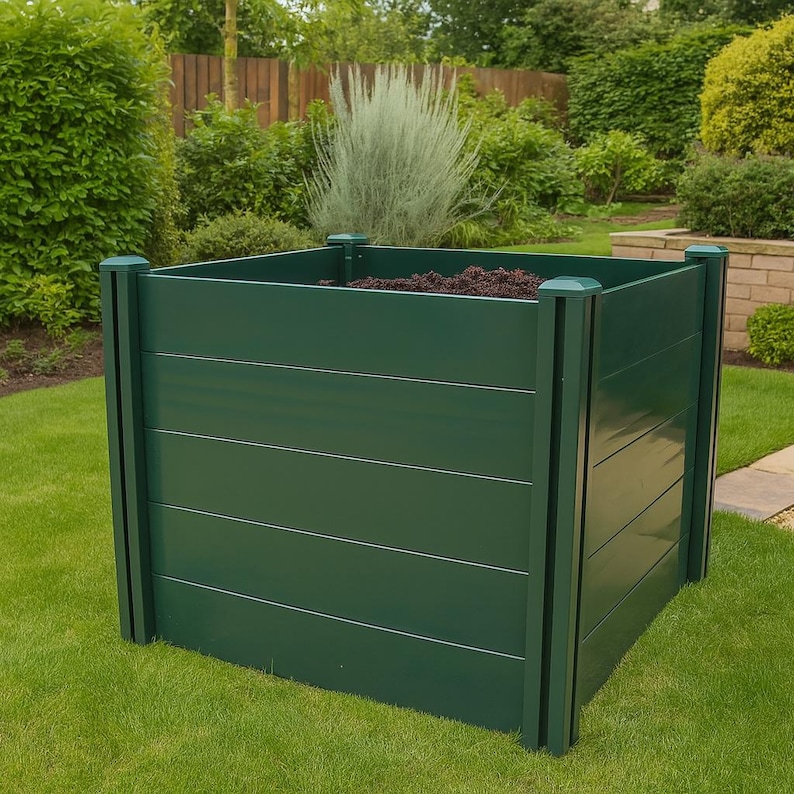 May include: A dark green, square raised garden bed with horizontal wooden planks. The bed is filled with soil and sits on a green lawn. The corners have vertical supports and decorative caps.