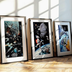 May include: Three framed Star Wars art prints. The prints depict space battles with spaceships, planets, and the Death Star. The frames are black with white mounts, leaning against a white wall on a wooden floor.