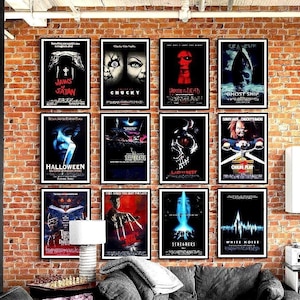 Twelve framed horror movie posters arranged in a grid on a brick wall above a dark grey sectional sofa with blankets, a wooden coffee table and a striped armchair in a cozy living room.