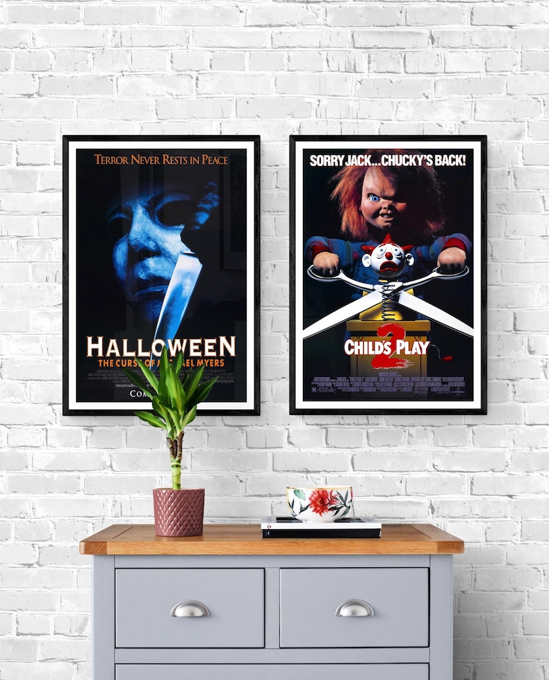 Two movie posters on a white brick wall. The poster on the left is for the movie "Halloween" and features a close-up of Michael Myers' face. The poster on the right is for the movie "Child's Play 2" and features Chucky holding a pair of scissors.