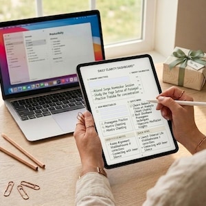 May include: A laptop and tablet are on a wooden surface. The tablet displays a "Daily Clarity Dashboard" with notes. A gift box with a green ribbon and a few pencils and paperclips are also on the surface.
