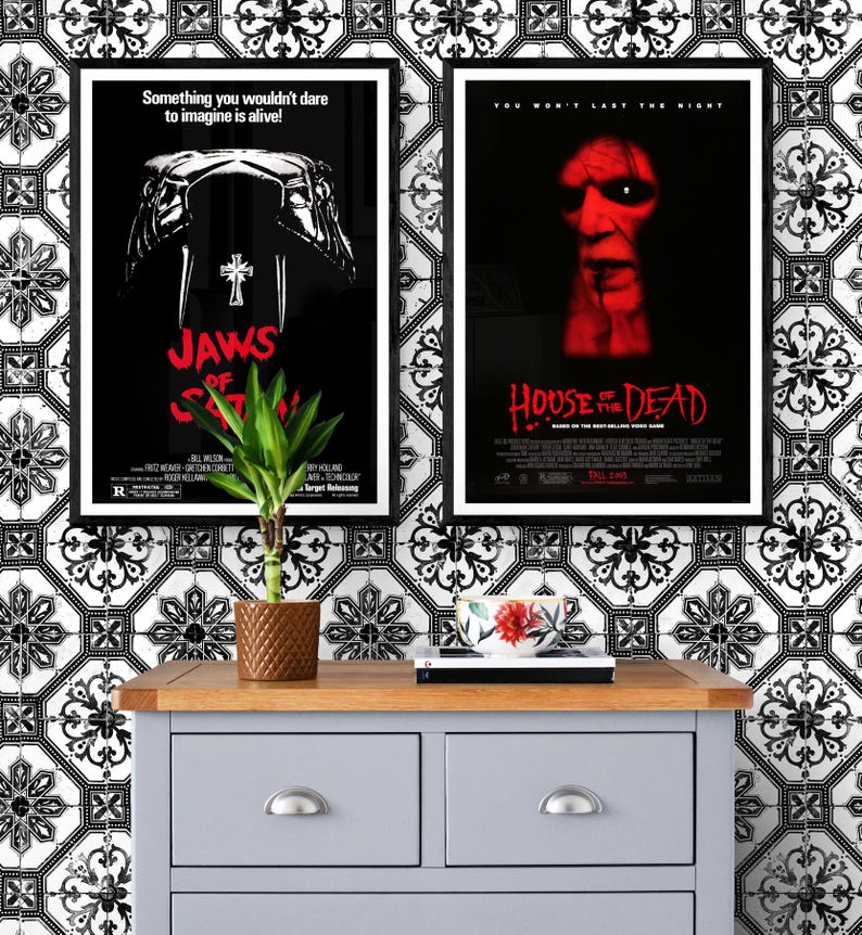 Two movie posters on a white and black tiled wall. The poster on the left is for the movie "Jaws of Satan" and the poster on the right is for the movie "House of the Dead".