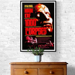 A black and red movie poster for the horror film "House of 1000 Corpses" directed by Rob Zombie. The poster features a close-up of a man's face with blood and gore, and the title of the film in large, bold letters.