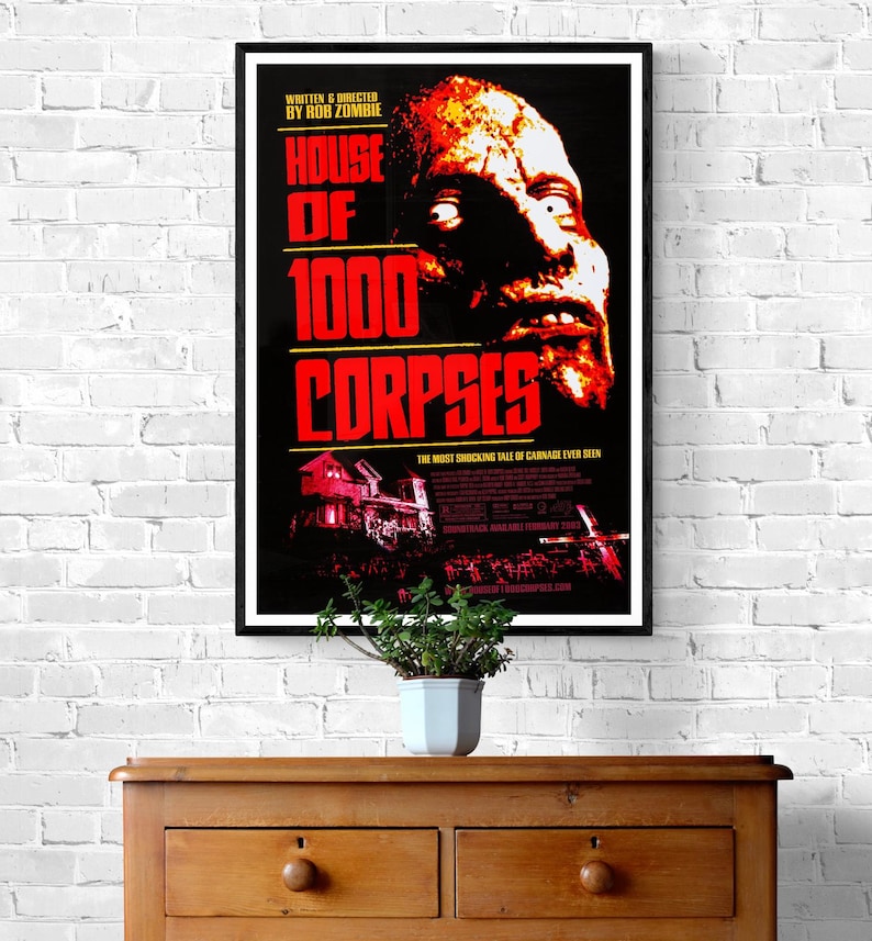 A black and red movie poster for the horror film "House of 1000 Corpses" directed by Rob Zombie. The poster features a close-up of a man's face with blood and gore, and the title of the film in large, bold letters.