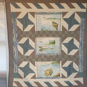 May include: A large, rectangular quilt with a nature theme. The quilt features three rectangular panels with landscape scenes labeled "Stream", "Lake", and "Pond". The quilt has a star pattern in blue and white, with a brown and tan border.