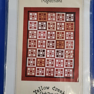 May include: A quilting pattern titled "Reflections" by Yellow Creek Quilt Designs. The pattern features a red, white, and yellow quilt with a geometric design. The pattern is available for purchase from Yellow Creek Quilt Designs.