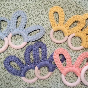 May include: Five crocheted teething rings with wooden centers. The rings are in shades of blue, yellow, and pink.