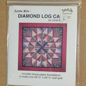 May include: A package for a "Diamond Log Cabin" wall quilt pattern by Cindi E. The pattern includes tissue paper foundations to make a 26 1/2" x 26 1/2" quilt. The quilt design features a colorful starburst pattern in pink, blue, and white.